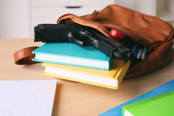 Mochila escolar con libros, papelería y pistola en el escritorio —  Fotos de Stock