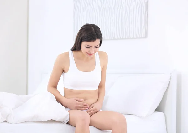 Wanita hamil cantik yang menderita sakit perut duduk di tempat tidur — Stok Foto