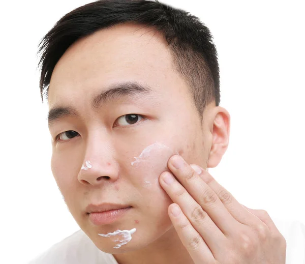 Jeune homme asiatique appliquant la crème pour la peau de problème sur le visage, sur fond blanc — Photo