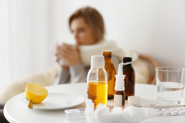 Limón, medicamentos y termómetro electrónico con mujer enferma borrosa en el fondo — Foto de Stock