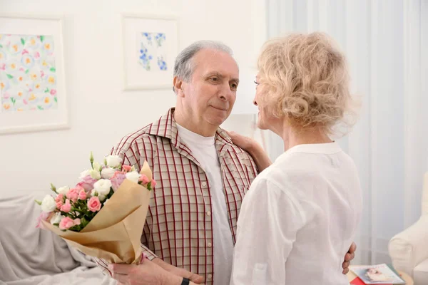 Glückliches Senioren-Paar mit Blumen tanzt zu Hause — Stockfoto