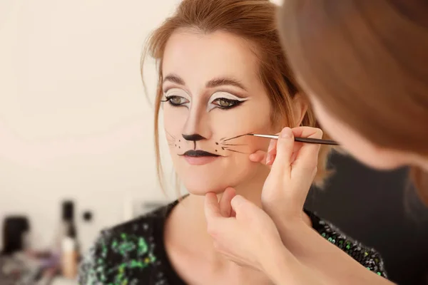 Visagiste applying cat makeup onto face of beautiful young woman in salon — Stock Photo, Image