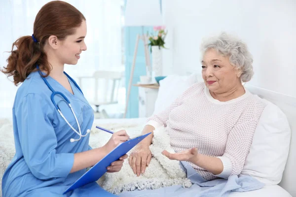 Медсестра розмовляє з літньою жінкою в світлій кімнаті — стокове фото