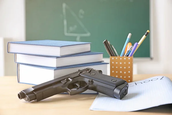 Школьные канцтовары и пистолет на столе в классе — стоковое фото