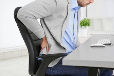 Man with back pain in armchair at office, closeup