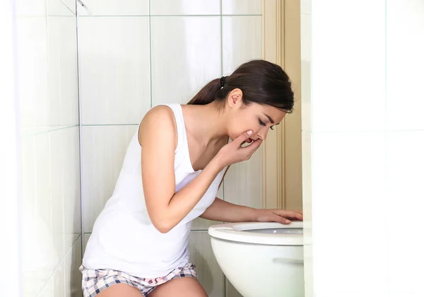 Mujer joven vomitando cerca del inodoro en casa —  Fotos de Stock
