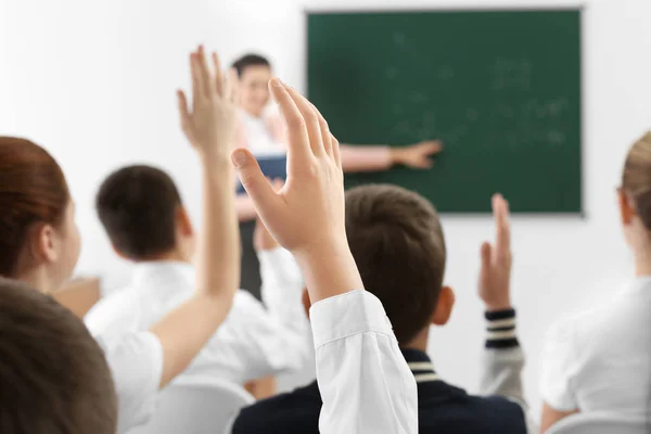 Schoolkinderen verhogen handen voor antwoord tijdens de les — Stockfoto