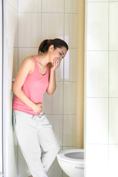 Young vomiting woman near toilet bowl at home