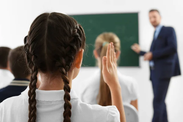 Schoolmeisje hand opsteken voor antwoord tijdens de les — Stockfoto