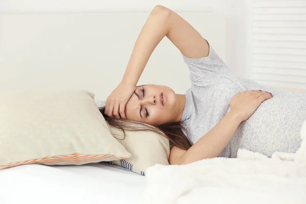 Unga gravid kvinna lider av huvudvärk liggandes i sängen hemma — Stockfoto