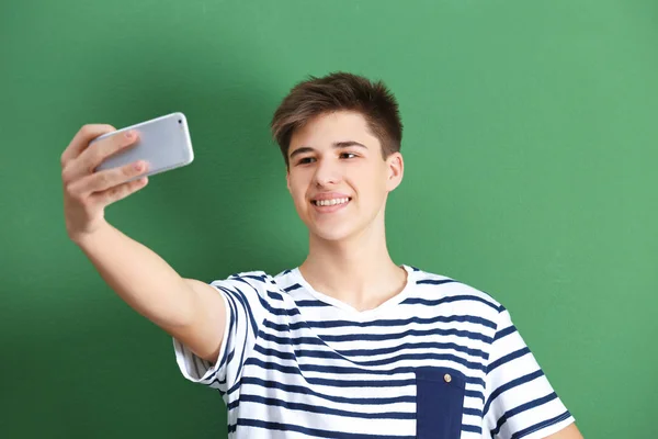 Nastoletni chłopiec podejmowania selfie z telefonu komórkowego na kolor tła — Zdjęcie stockowe