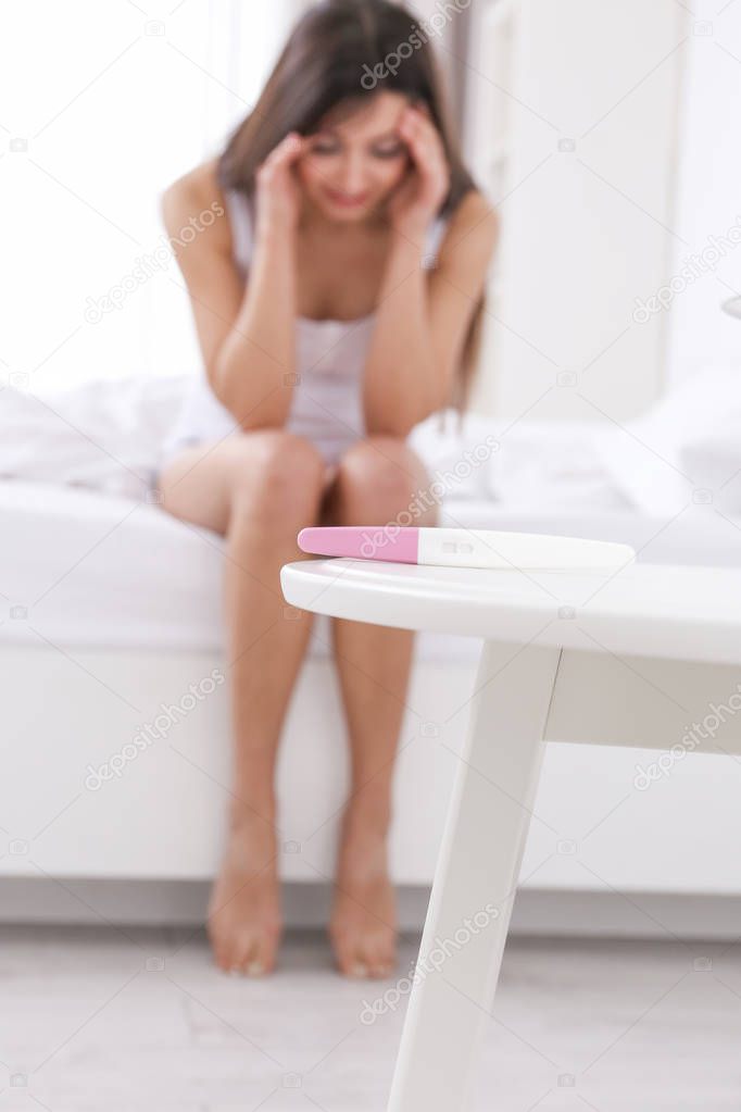 Pregnancy test and blurred woman suffering from headache on background