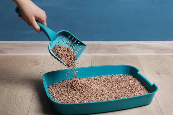 Woman cleaning litter box with scoop on floor