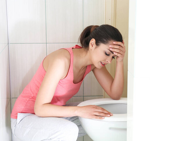 Young vomiting woman near toilet bowl at home