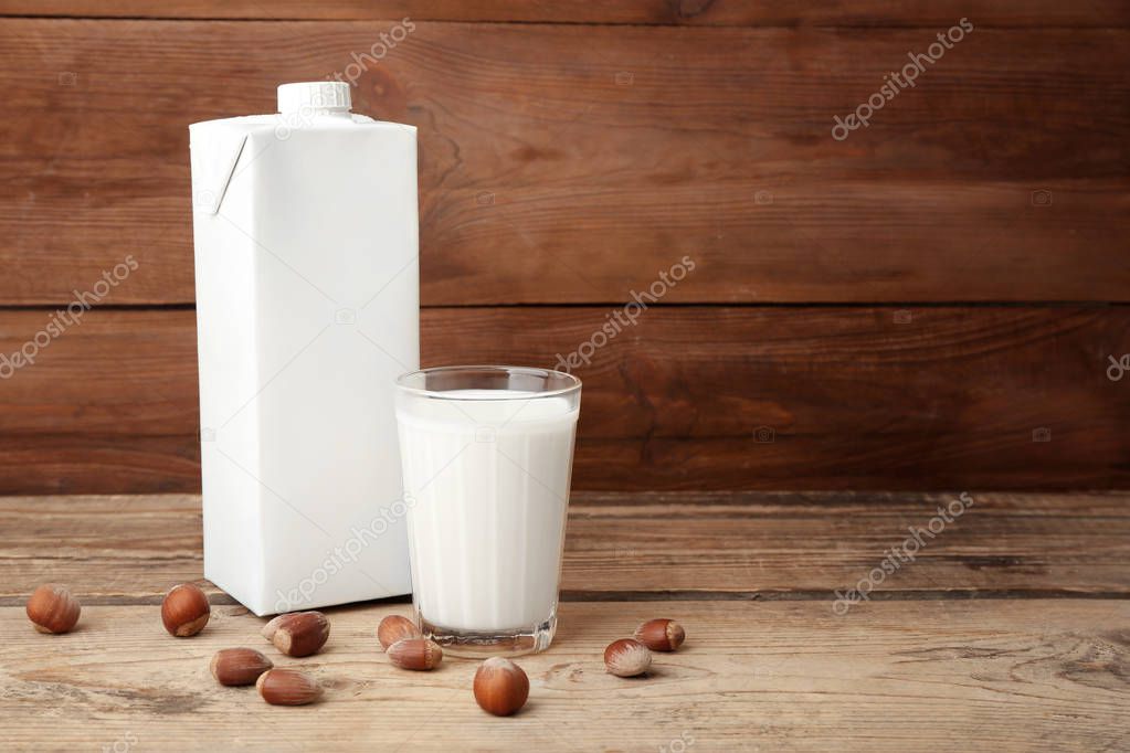 Carton box and glass of milk on wooden background