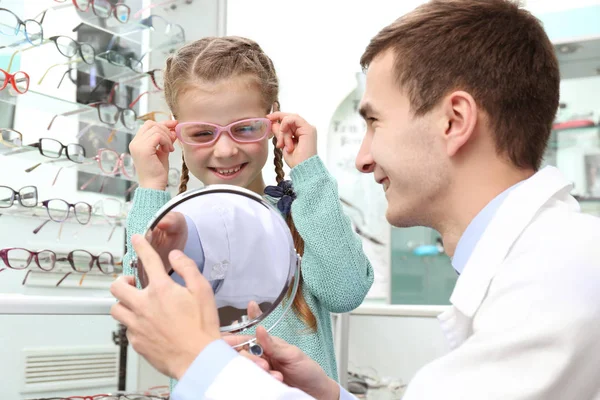 Giovane medico aiuta la bambina a scegliere nuovi occhiali nel negozio — Foto Stock