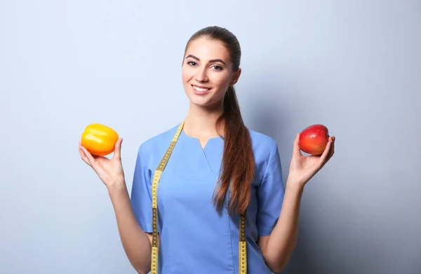 Unga kvinnliga nutritionist på ljus färgbakgrund — Stockfoto