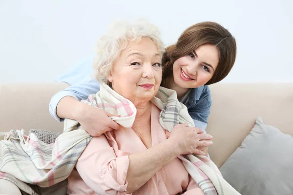 Hermosa chica que cubre la abuela con manta en el sofá en casa —  Fotos de Stock