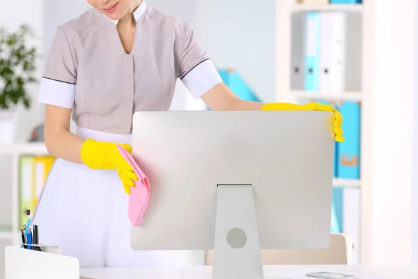 Beautiful chambermaid cleaning computer monitor at office — Stock Photo, Image