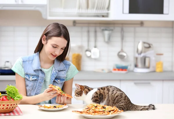Молодая женщина и милый кот едят вкусную пиццу на кухне — стоковое фото