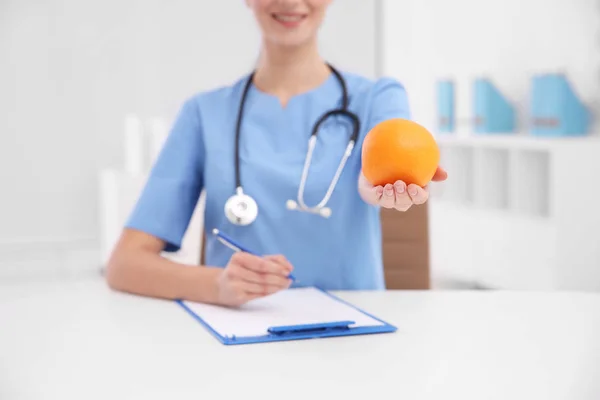 Nutricionista femenina con naranja sobre fondo borroso, primer plano — Foto de Stock