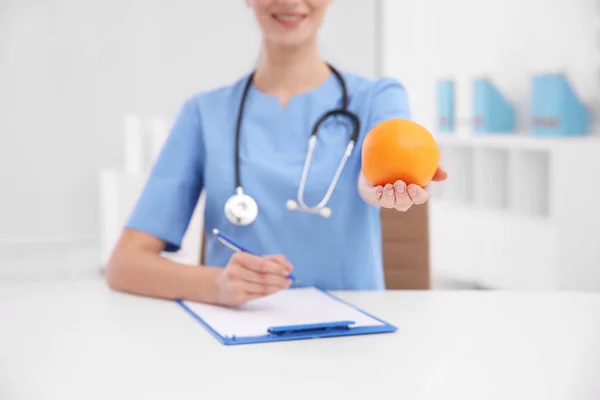 Ernährungsberaterin mit Orange auf verschwommenem Hintergrund, Nahaufnahme — Stockfoto