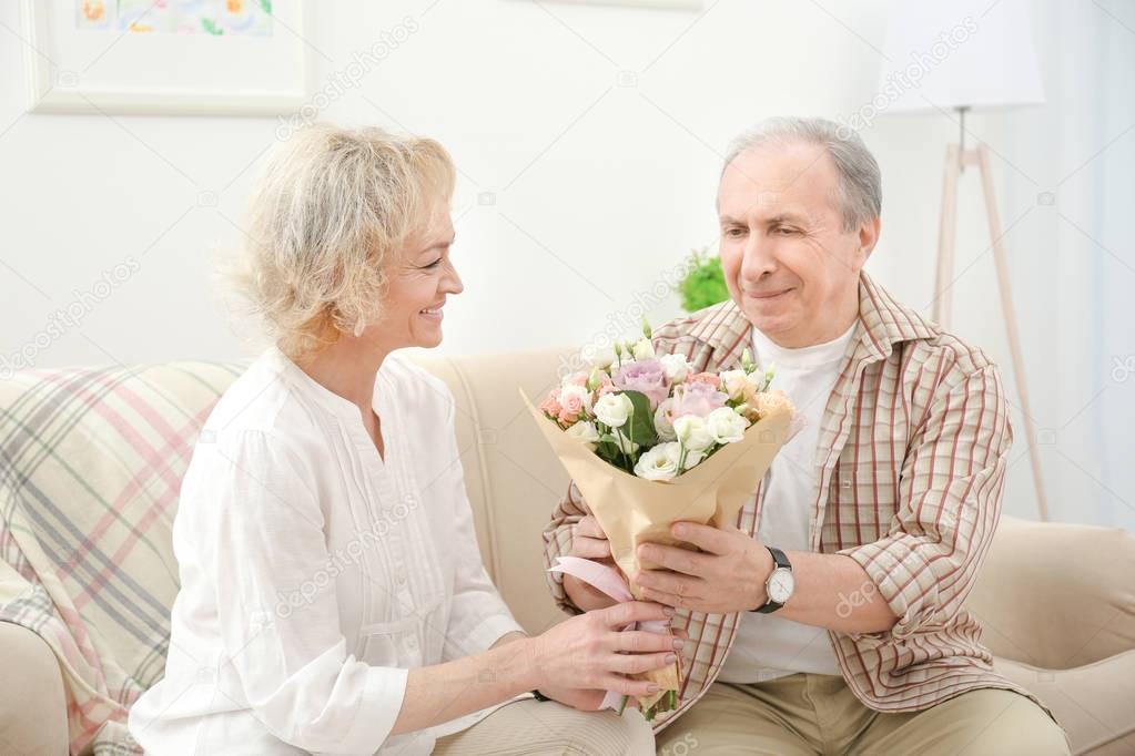 Senior man giving flowers to his wife at home
