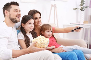 Mutlu bir aile evdeki kanepede televizyon izliyor.