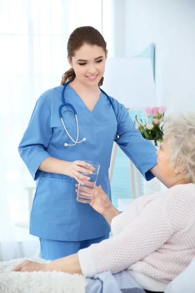 Verpleegkundige glas water geven aan oudere vrouw — Stockfoto