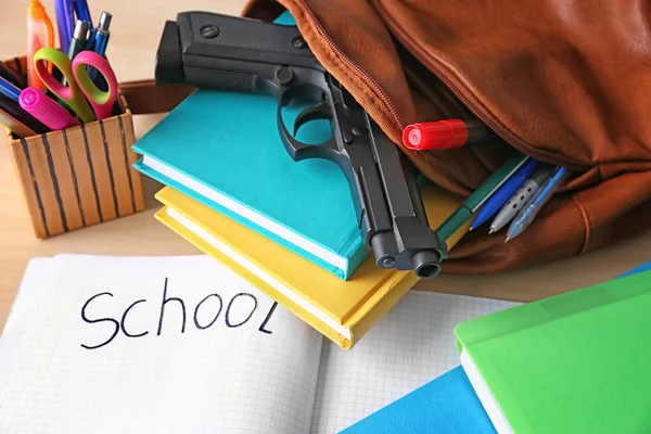 Школьный рюкзак с книгами, канцелярскими принадлежностями и пистолетом на столе — стоковое фото
