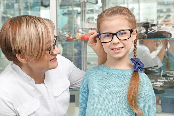 Doctor ayudando a la niña a elegir nuevas gafas en la tienda —  Fotos de Stock