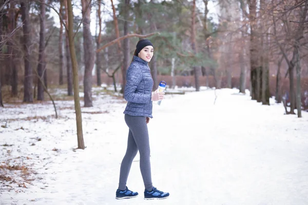 Молодая женщина в спортивной одежде с бутылкой на фоне зимнего парка — стоковое фото