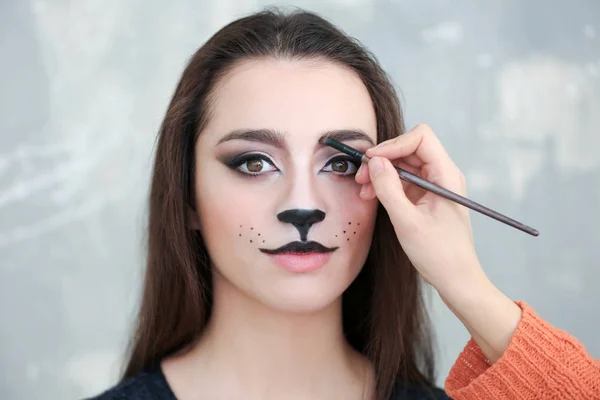 Visagiste aplicando maquillaje de gato sobre la cara de una hermosa joven en el salón — Foto de Stock