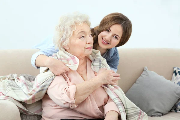 Beautiful girl covering grandmother with blanket on couch at home — Stock Photo, Image