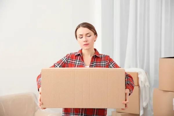 Mujer joven sosteniendo pesada caja en la habitación — Foto de Stock