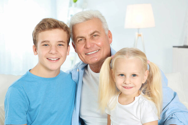 Cute children with grandfather sitting on sofa in living room