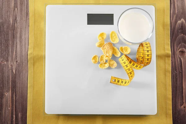 Glass of milk with cornflakes on scales — Stock Photo, Image