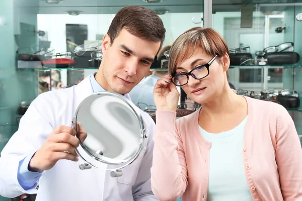 Ung läkare att hjälpa kvinnan att välja nya glasögon i butiken — Stockfoto