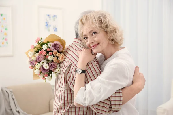 Mulher sênior feliz com buquê de flores abraçando seu marido — Fotografia de Stock