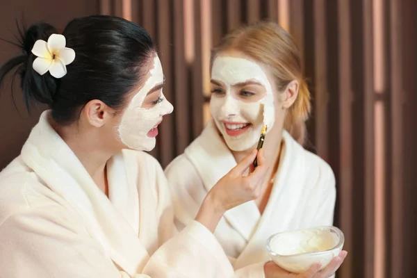 Güzel genç kadın maskesi spa salonu arkadaşının yüzüne üzerine uygulama — Stok fotoğraf