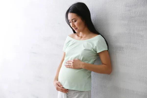 Έγκυος γυναίκα της Ασίας που στέκεται κοντά φωτός τοίχο — Φωτογραφία Αρχείου