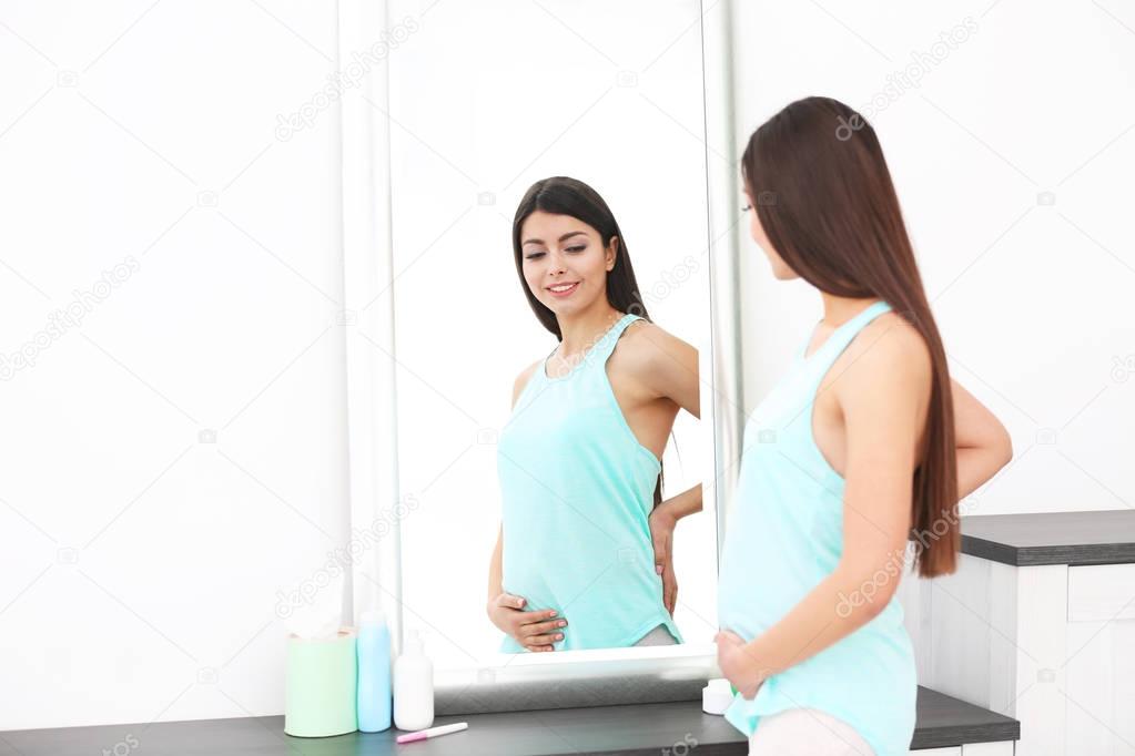 Beautiful pregnant woman looking in mirror at home