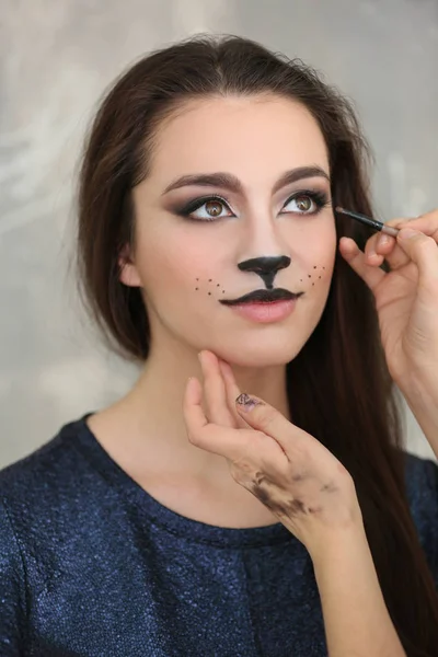 Visagiste applying cat makeup onto face of beautiful young woman in salon — Stock Photo, Image