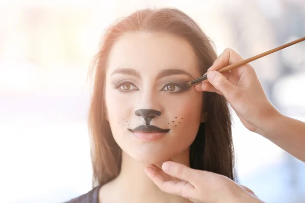 Visagiste aplicando maquillaje de gato sobre la cara de una hermosa joven en el salón — Foto de Stock