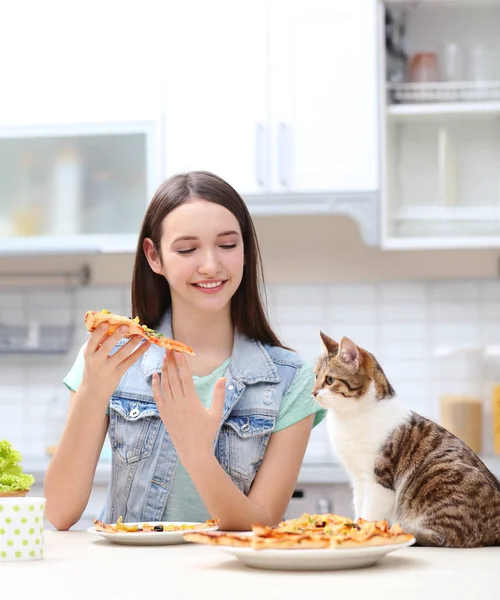 Mladá žena a roztomilé kočky jíst chutné pizzy v kuchyni — Stock fotografie