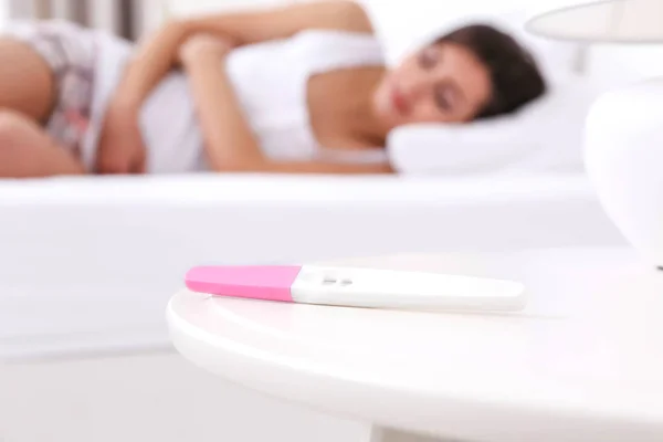 Pregnancy test and blurred woman lying in bed on background — Stock Photo, Image