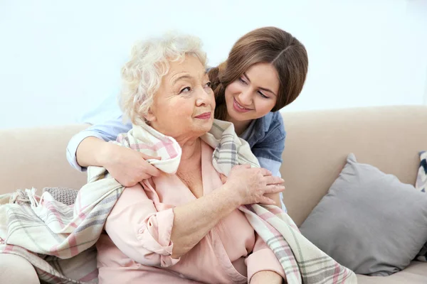 Beautiful girl covering grandmother with blanket on couch at home — Stock Photo, Image