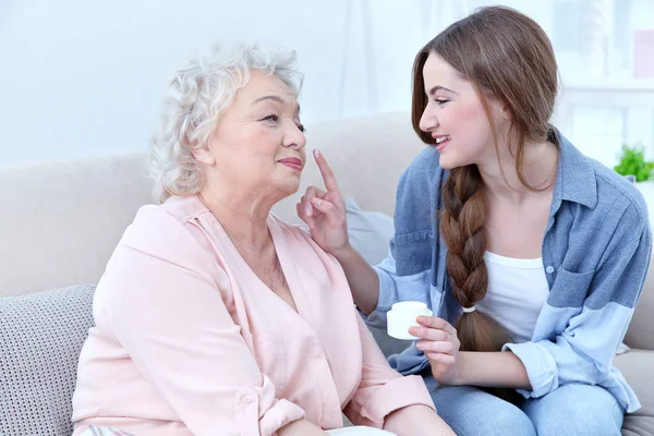 Mooi meisje en grootmoeder huidverzorging overneemt couch thuis — Stockfoto