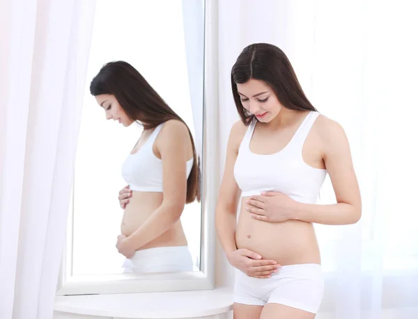 Mulher grávida bonita olhando para a barriga na sala de luz — Fotografia de Stock