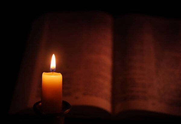 Burning candle and Bible on background